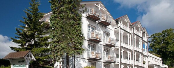 A multi-story hotel with balconies, a sign indicating it's a hotel, and surrounding trees.