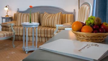 Ein Zimmer mit einer Couch, zwei Sesseln, einem kleinen Tisch mit einer Lampe, einer Obstschale und einem Buch auf einem Tisch.