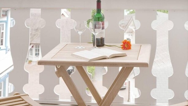 A balcony with a table set for two, a bottle of wine, and an open book. - Hotel Stranddistel Rügen (Göhren)