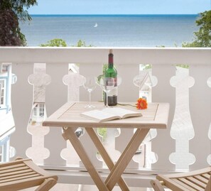 Varanda com mesa posta para dois, uma garrafa de vinho e um livro aberto.