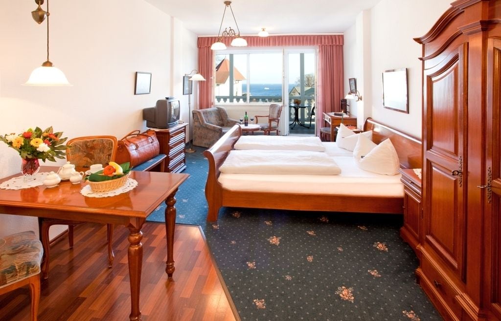 Habitación de hotel con cama, escritorio y silla, una mesita con un florero, y vista al mar por la ventana.
