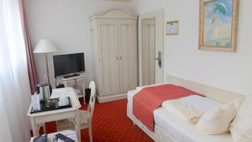 A hotel room with a bed, a desk with a TV, a wardrobe, and a painting on the wall.