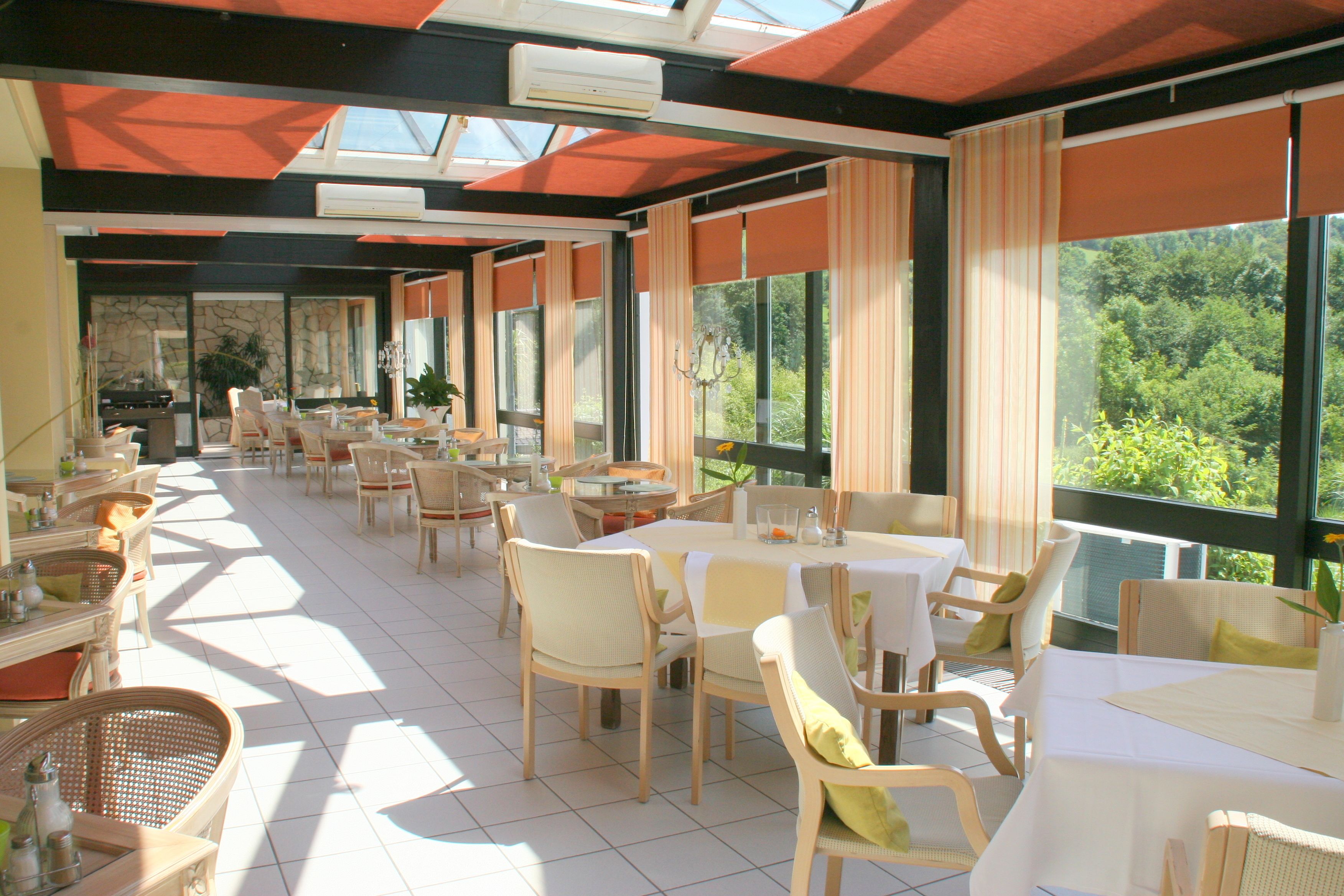 Un restaurant spacieux, doté de nombreuses tables et chaises, de grandes fenêtres offrant une vue sur la verdure et d’un aménagement intérieur moderne.