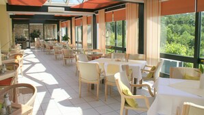 A spacious restaurant with multiple tables and chairs, large windows offering a view of greenery, and a modern interior design. - Sure Hotel by Best Western Rhoen Garden (Poppenhausen)