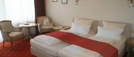 A hotel room with a double bed, two armchairs, a small round table, and a red carpet.