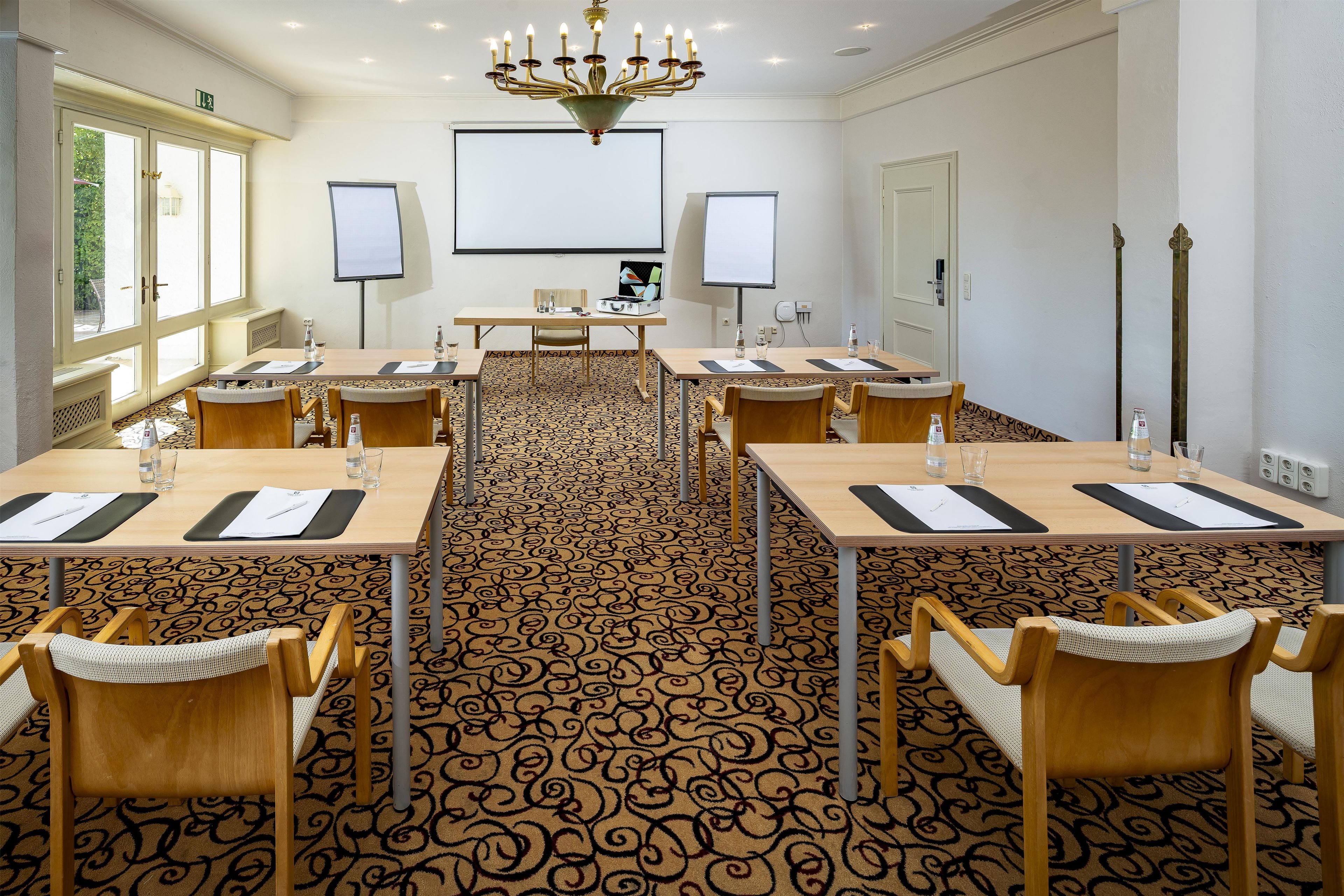 A conference room with a large carpeted floor, wooden tables, and chairs, equipped with water bottles and notepads.