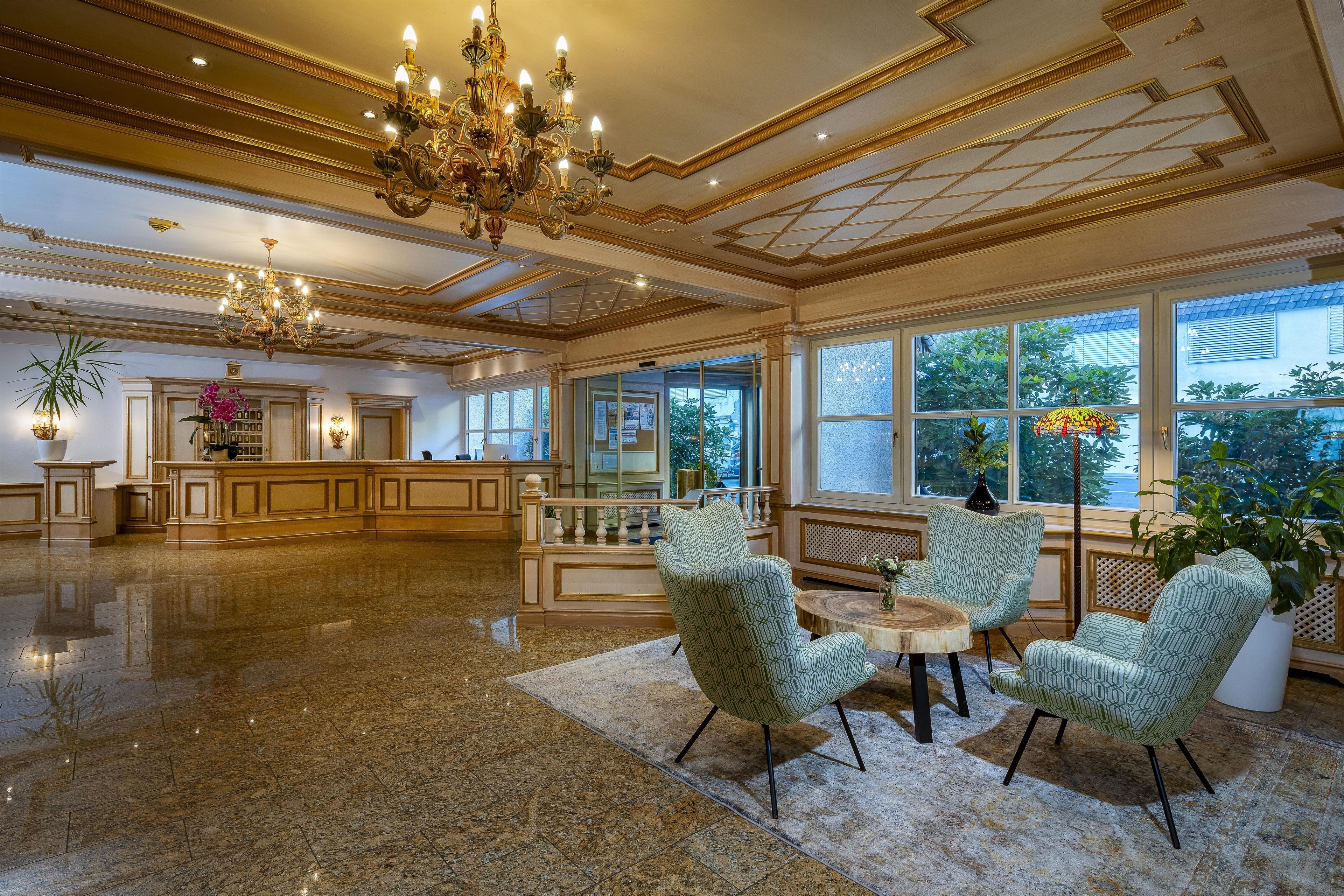 Eine geräumige Lobby mit einem prunkvollen Kronleuchter, einem Empfangstresen und großen Fenstern mit Blick ins Freie.