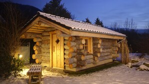 A log cabin with a wooden door and window, surrounded by snow and trees. - Sure Hotel by Best Western Rhoen Garden (Poppenhausen)