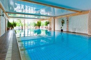 An indoor swimming pool with clear blue water, surrounded by potted plants and wooden beams.