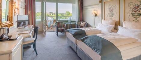 Habitación de hotel con cama, escritorio, silla, mesita y balcón con vista al paisaje.