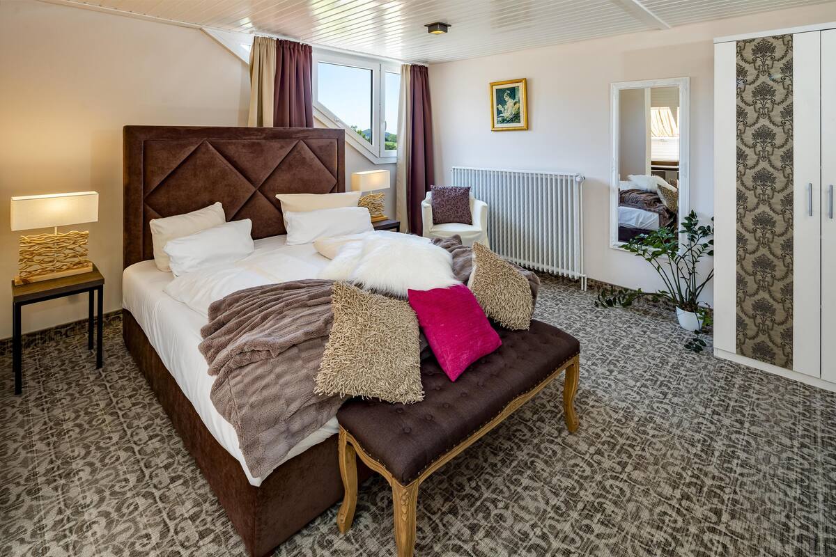 A well-appointed bedroom with a large bed, a bench, a chair, a bedside table, a radiator, and a wardrobe.