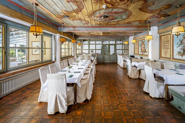 Un restaurante con una larga mesa dispuesta para comer, amplias ventanas y un techo decorativo.