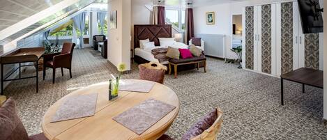 A hotel room with a bed, a dining area, a sofa, a TV, and a view of the outdoors.