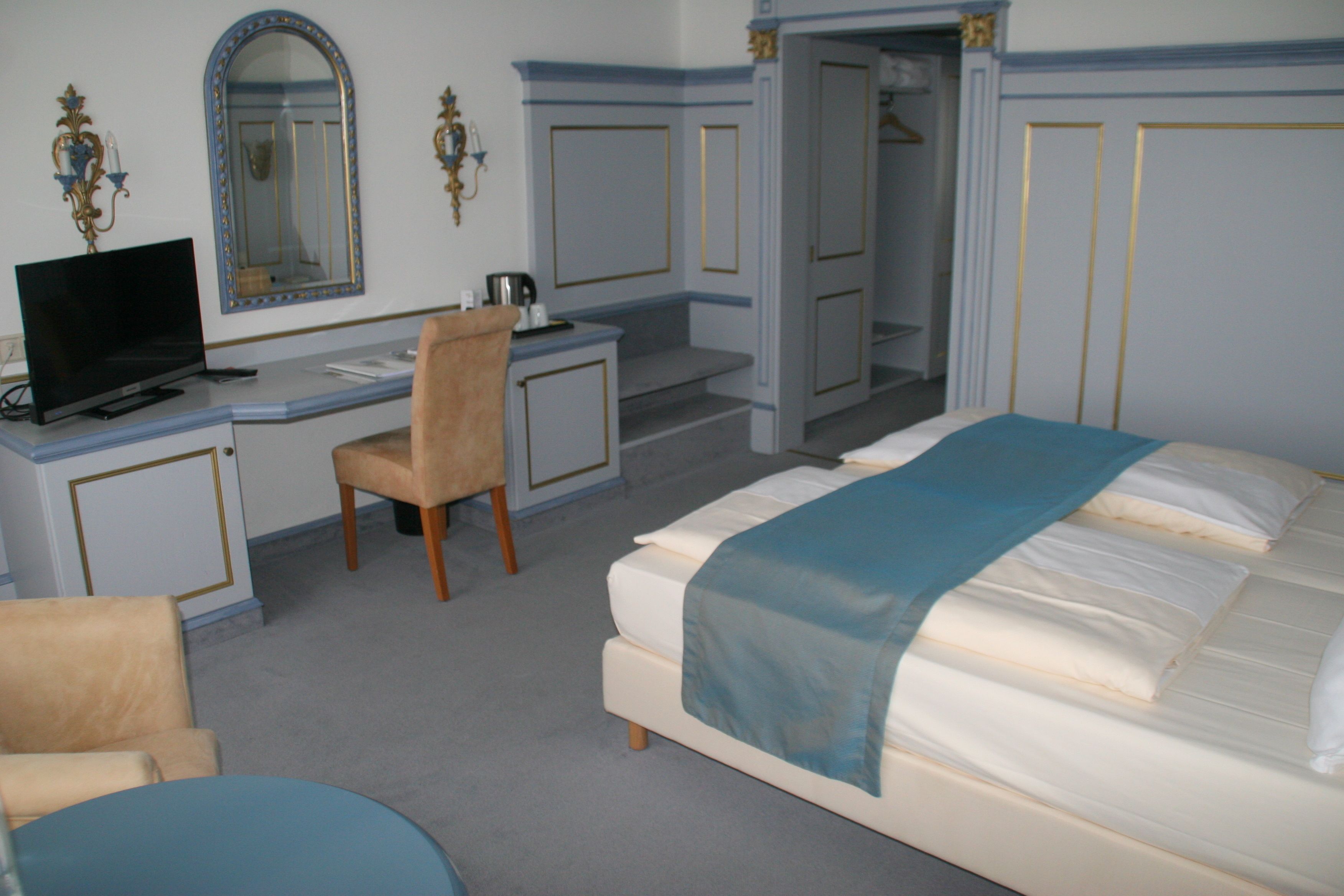Ein Hotelzimmer mit Bett, Schreibtisch, Stuhl, Fernseher und Spiegel.