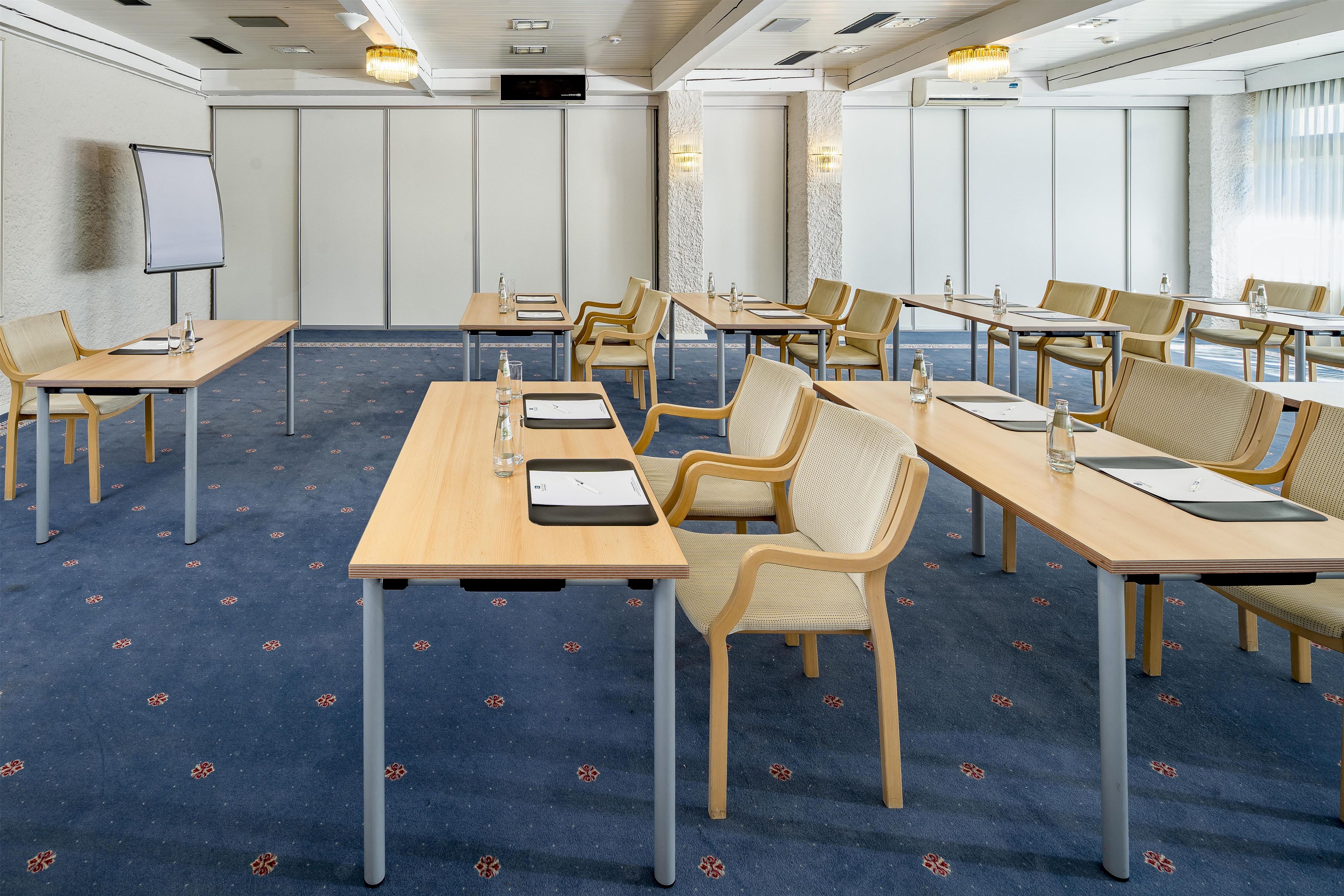 Un salón de conferencias con varias mesas y sillas, una pizarra y un ventanal que proporciona luz natural.