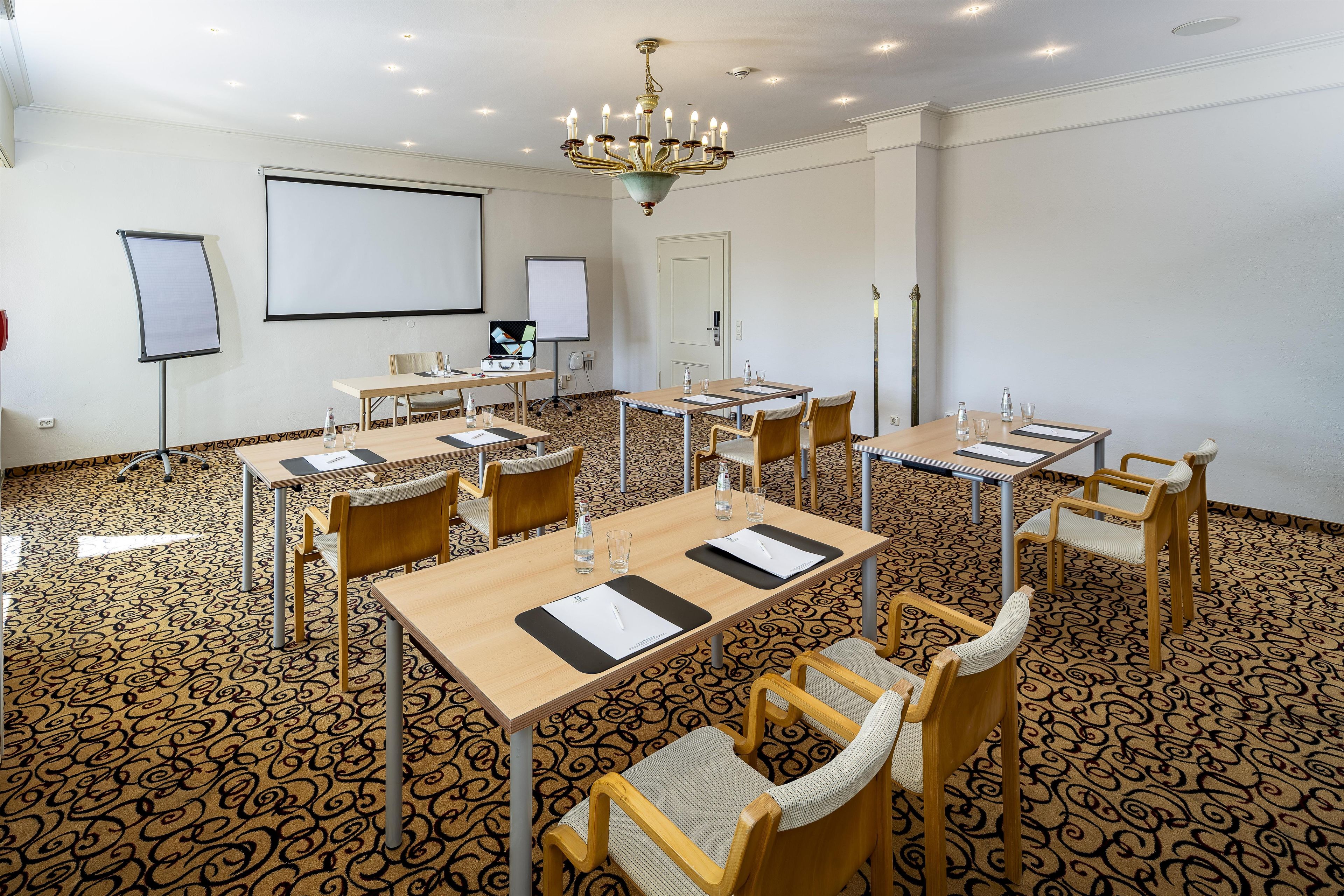 A conference room with multiple tables, chairs, a projector screen, and a whiteboard.