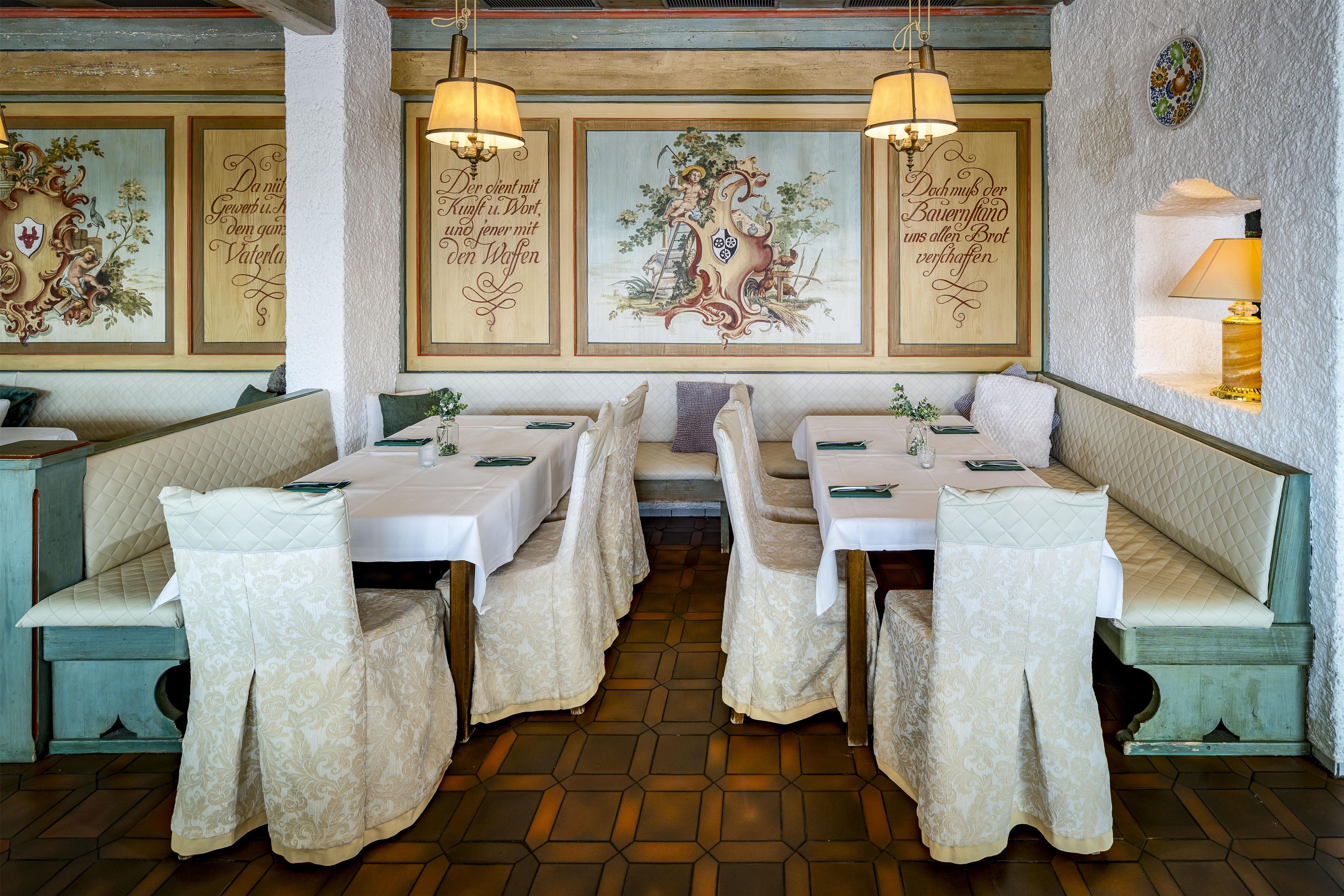 A restaurant with hexagonal tiled flooring, wooden benches with white tablecloths, and wall-mounted chandeliers.