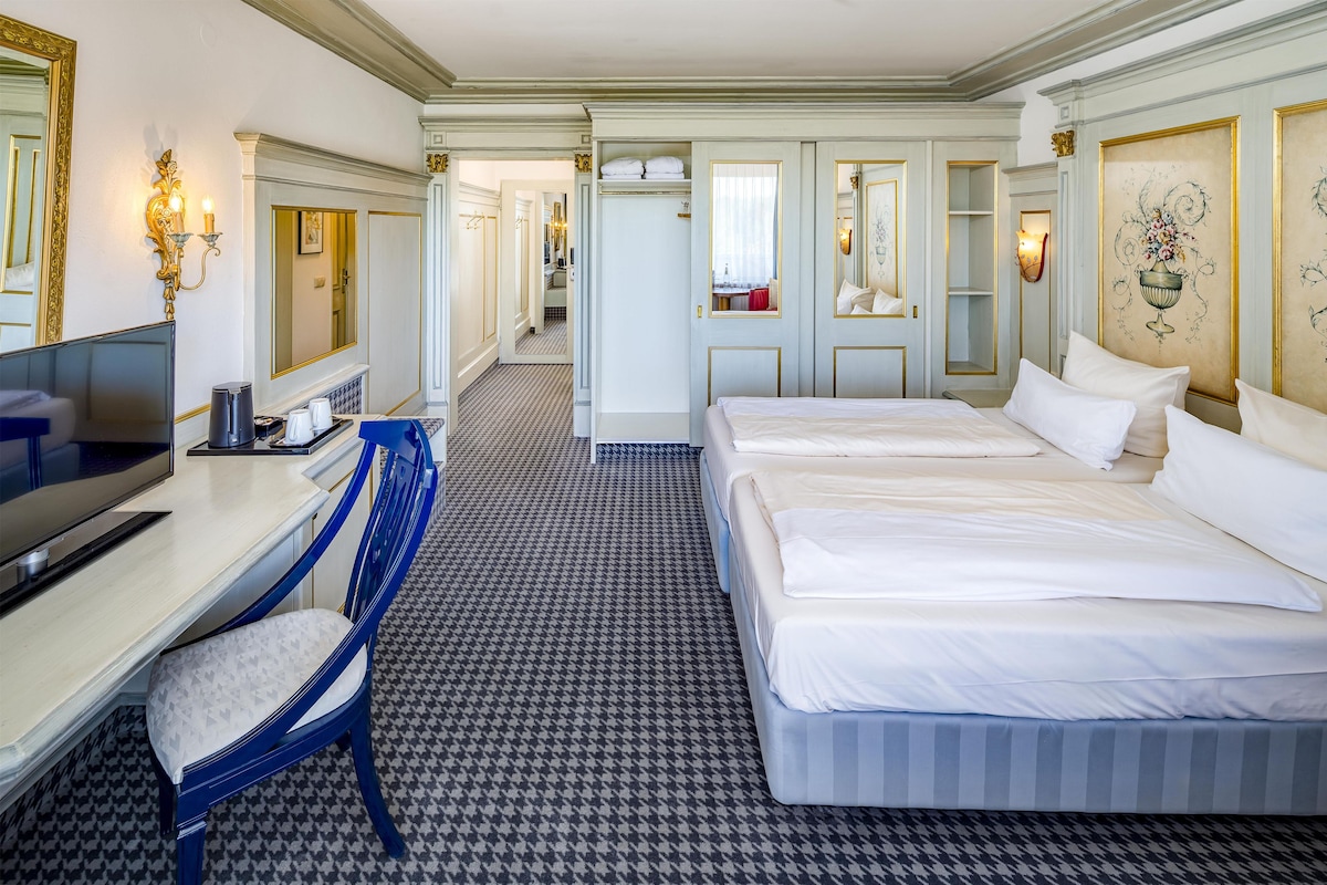 A hotel room with a large bed, a desk with a chair, a television, and a bathroom visible through an open door.