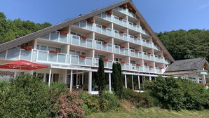 A multi-story hotel with balconies adorned with red flowers, a covered outdoor seating area, and lush greenery surrounding the building. - Sure Hotel by Best Western Rhoen Garden (Poppenhausen)