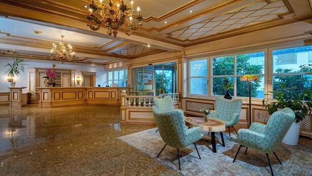 Een ruime lobby met een marmeren vloer, een receptiebalie en een zithoek met gestreepte stoelen.