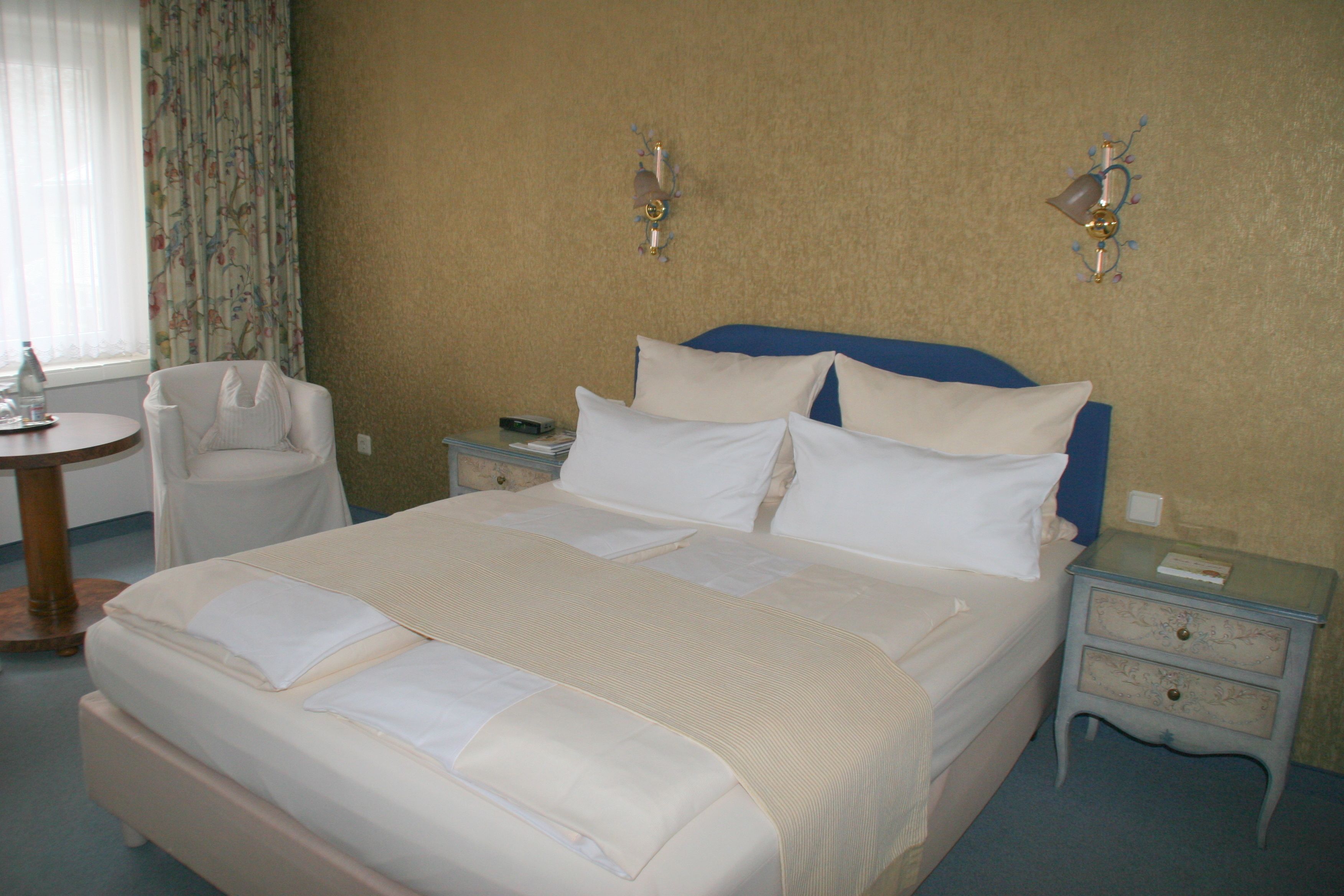A neatly made bed with white linens, a bedside table with a lamp, and a chair in a hotel room.