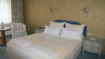 A neatly made bed with white linens, a bedside table with a lamp, and a chair in a hotel room.