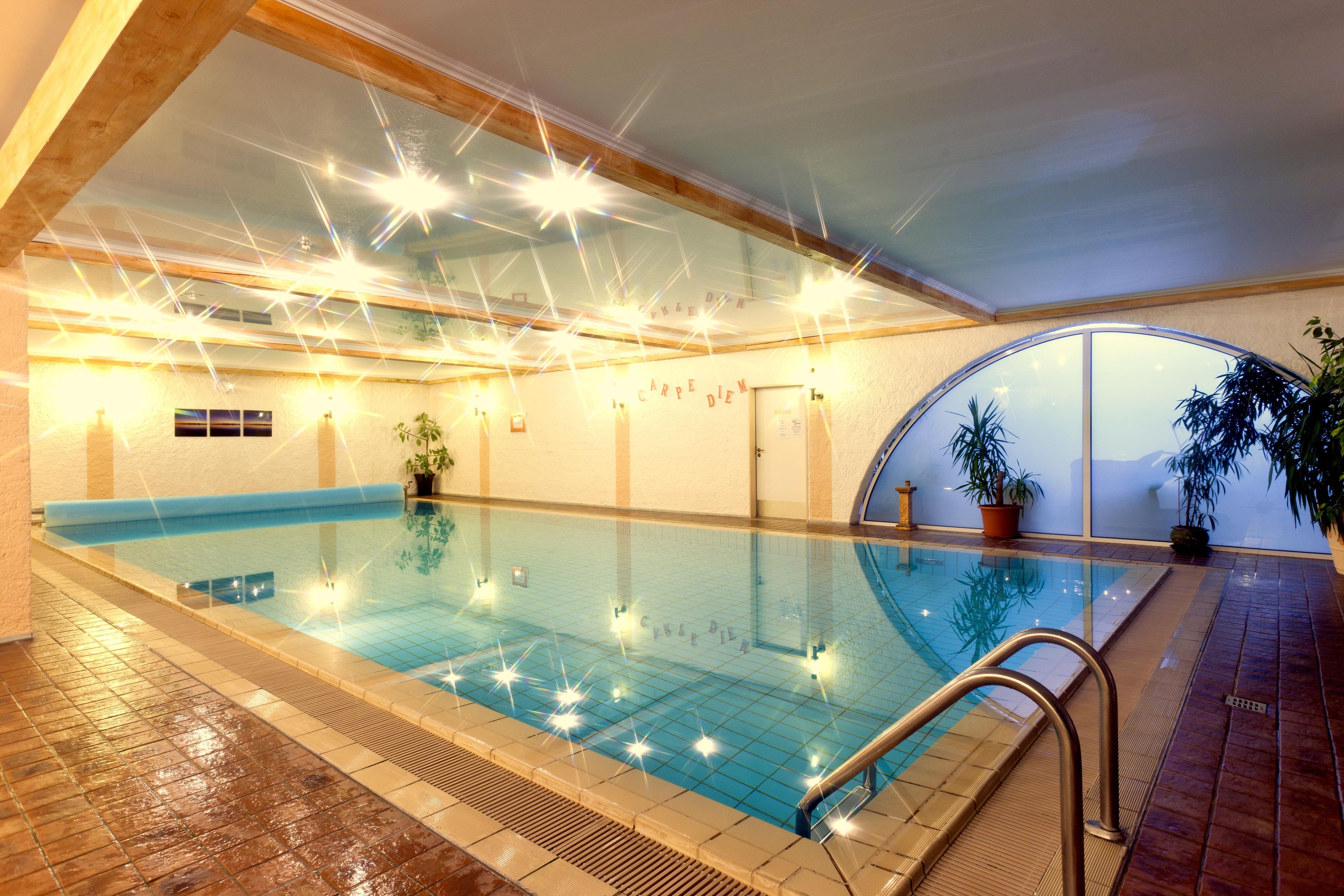 Piscina interna com água cristalina, paredes revestidas de azulejos e teto de madeira.
