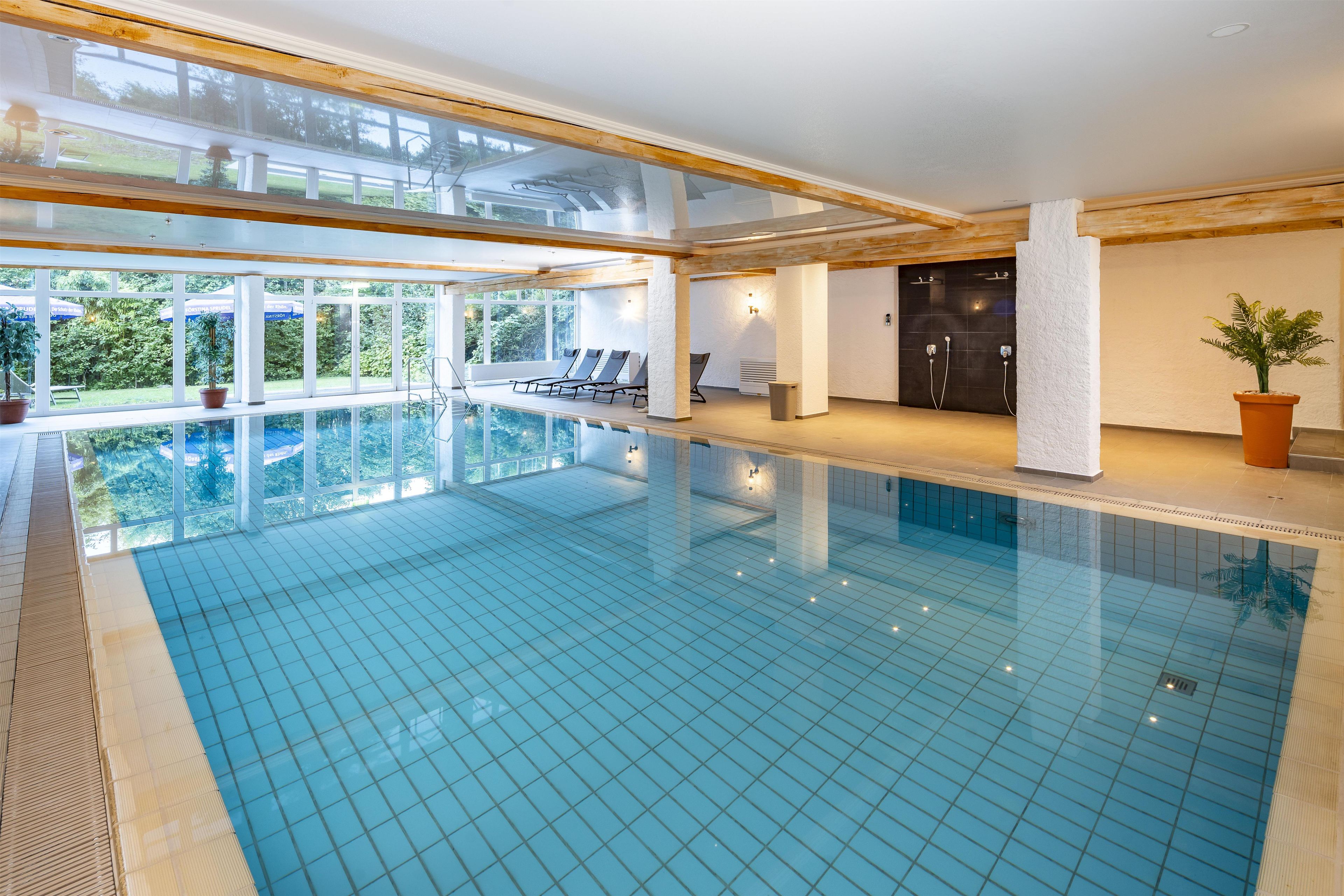A large indoor swimming pool with clear blue water, surrounded by windows and lounge chairs.
