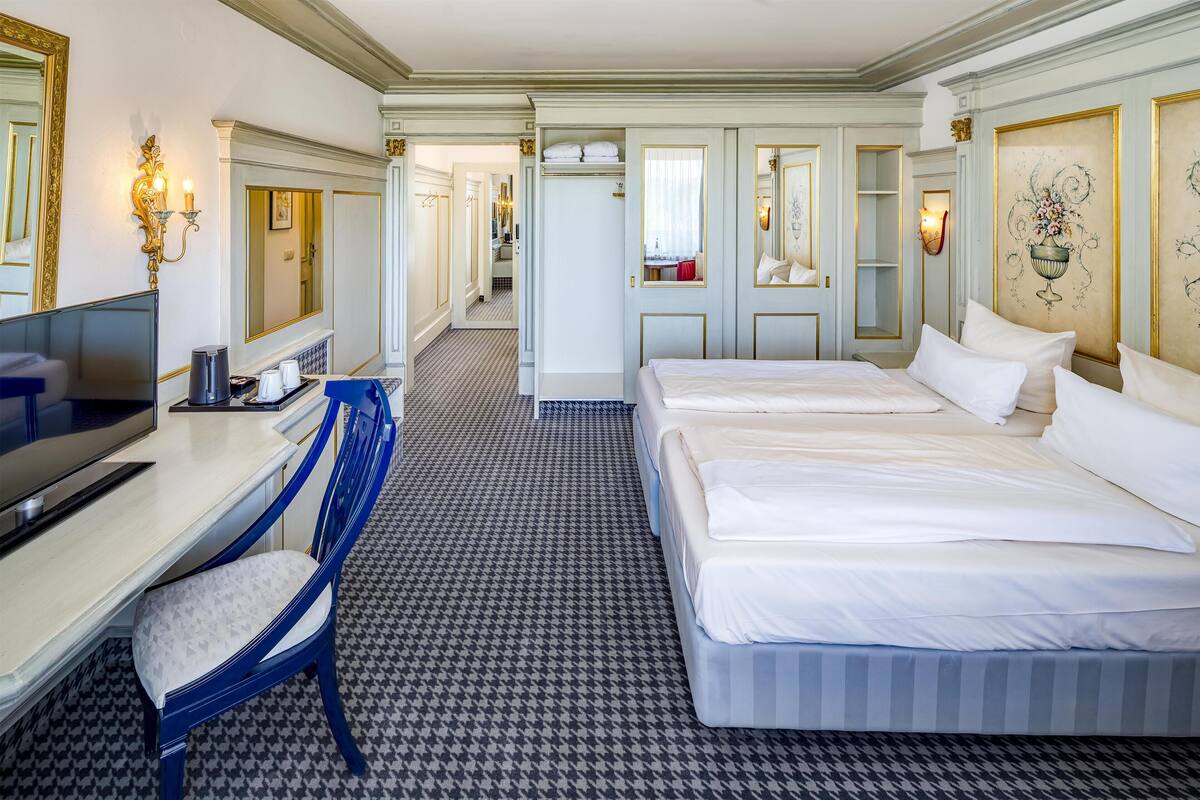 A hotel room with two beds, a desk with a TV, a chair, and a patterned floor.