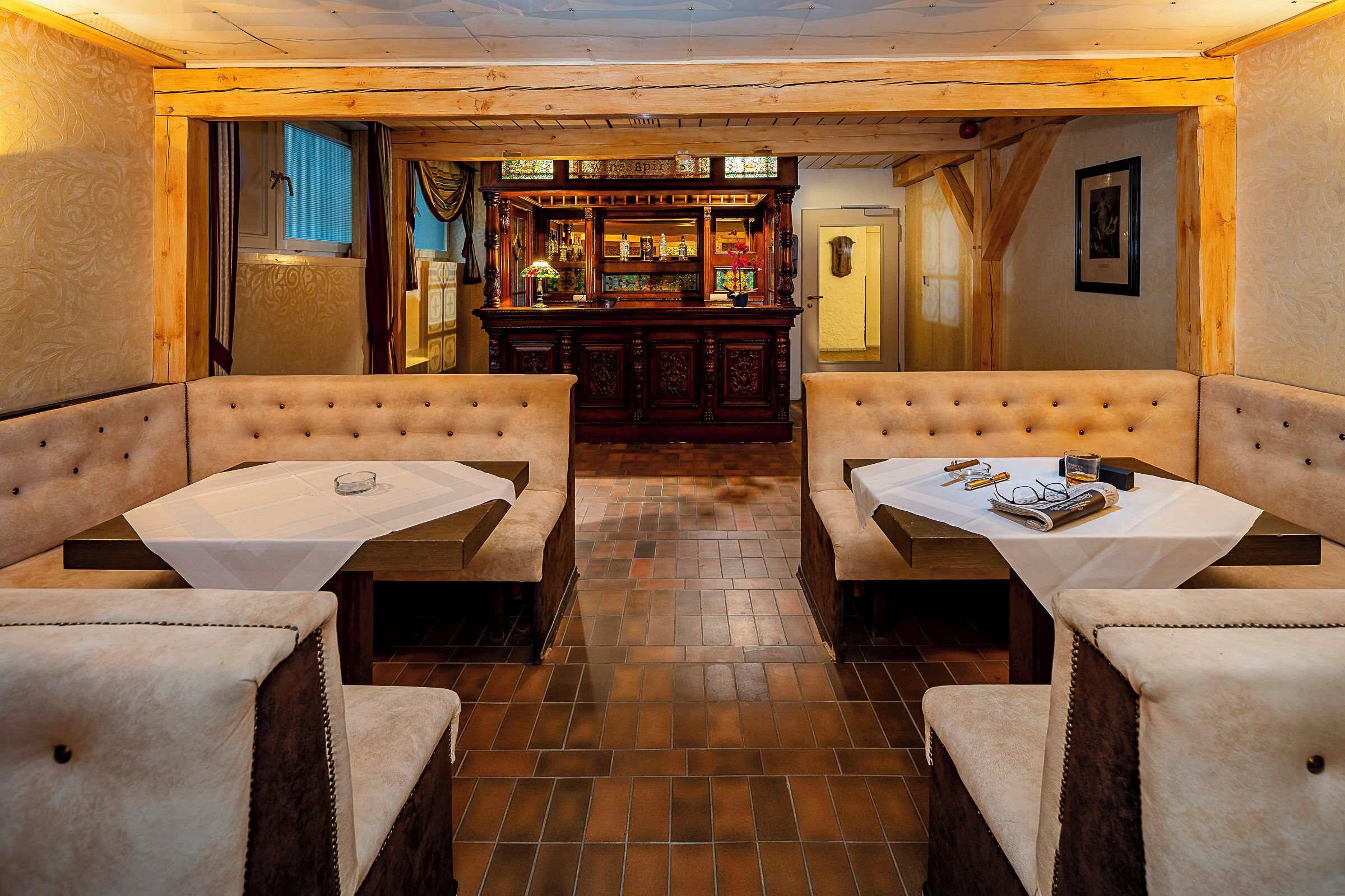 A cozy restaurant with two booths and a bar in the background.
