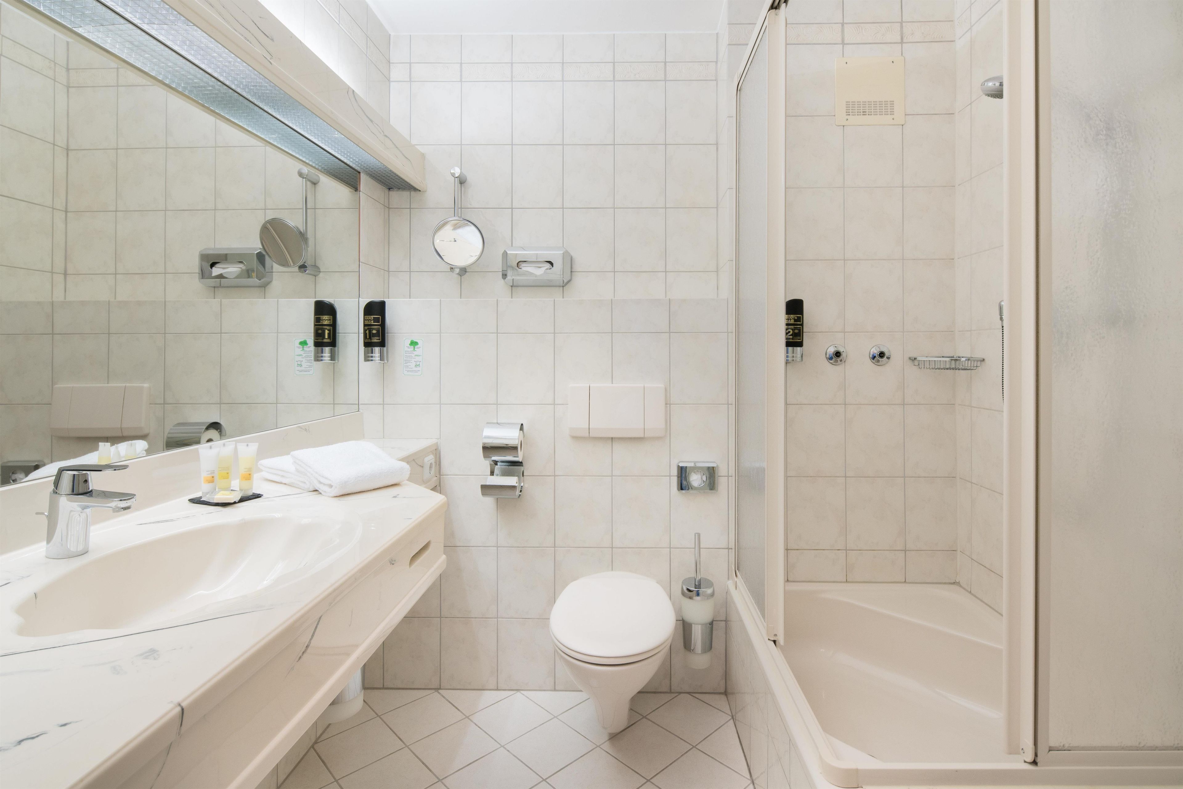 Une salle de bain moderne dotée d’un grand miroir, de deux lavabos, de toilettes et d’un espace douche.