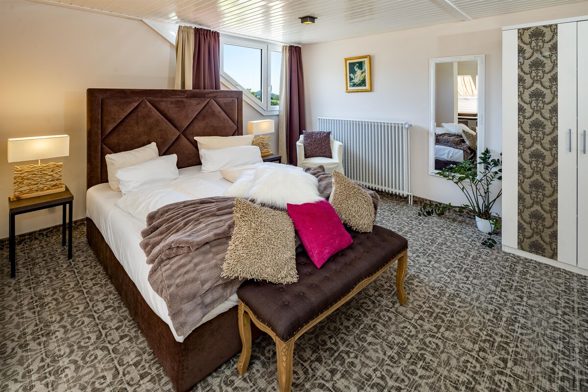 A well-appointed bedroom with a large bed, a bench, a chair, a bedside table, a radiator, and a wardrobe.
