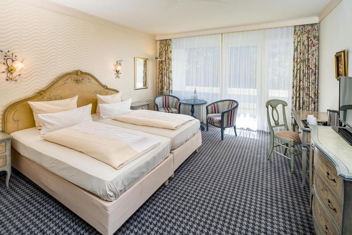 A hotel room with a large bed, two chairs, a small table, and a dresser.