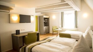 A hotel room with two beds, a desk, a chair, a TV, and a kitchenette. - Hotel Am Schloss (Heidelberg)