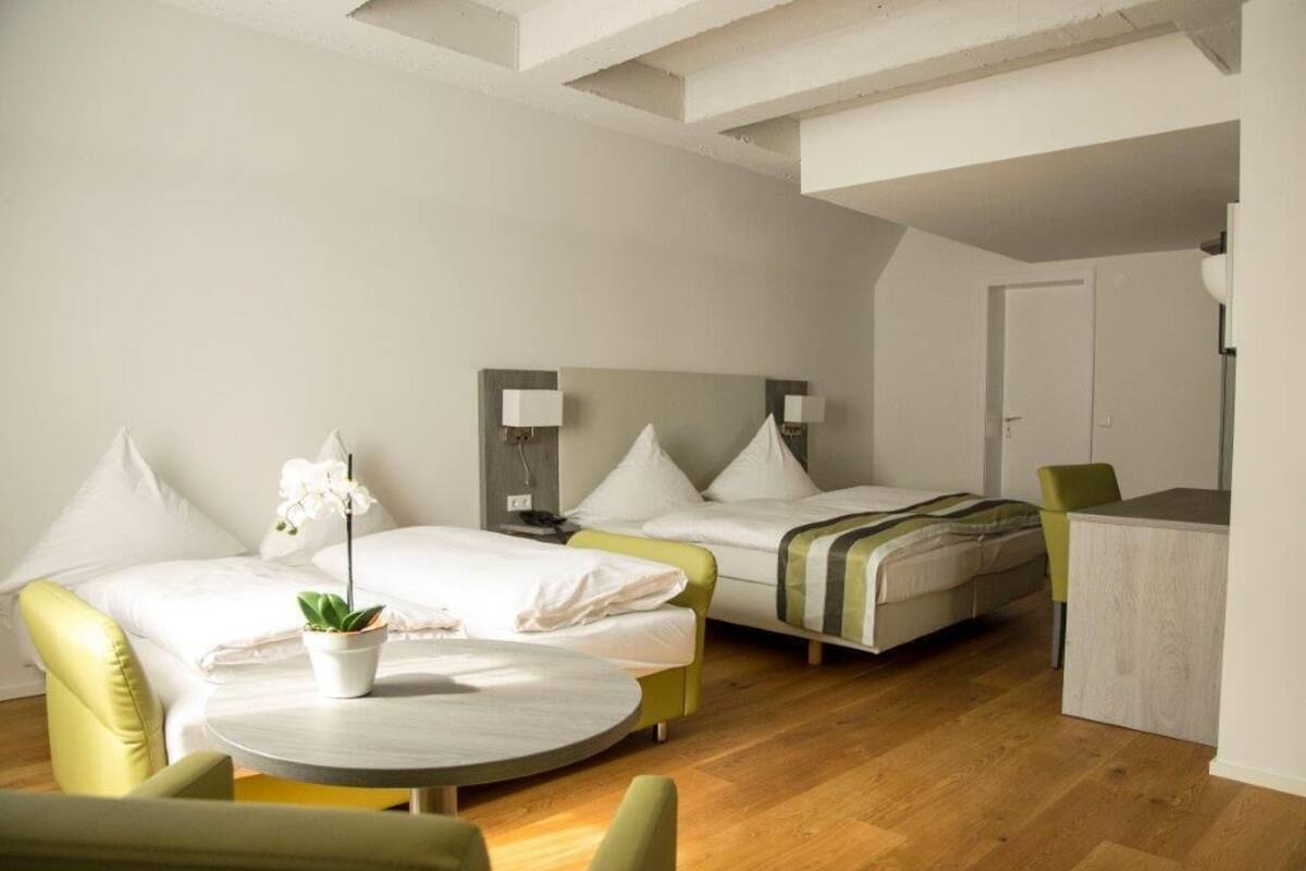 A hotel room with two beds, a desk, a chair, a round table, and a potted plant.