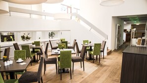 A modern dining area with wooden floors, green upholstered chairs, and a central staircase. - Hotel Am Schloss (Heidelberg)