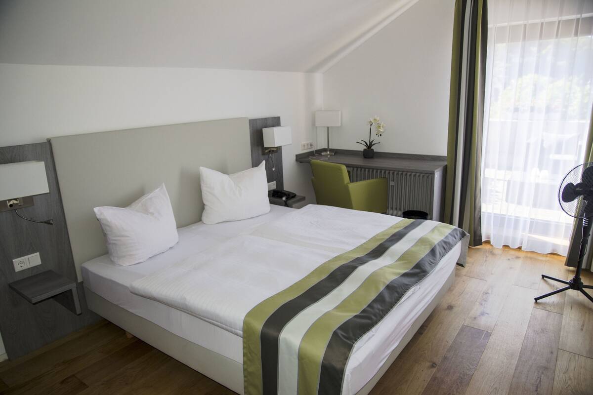 A hotel room with a bed, a desk, a chair, and a window with curtains.
