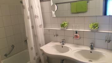 A bathroom with a white sink, a mirror, and a shower curtain. There are two shelves with toiletries and a green towel hanging on the wall.