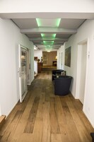 Een hal met houten vloer, een receptiebalie en een zithoek met een prullenbak.