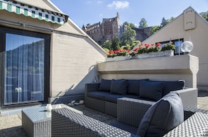Terraza en la azotea con mobiliario de mimbre, una puerta de vidrio y vistas a un castillo.