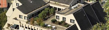 Un edificio de varios pisos con una terraza en la azotea, un pequeño jardín y un balcón visible.