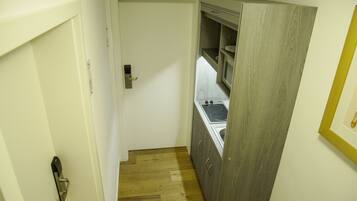 Un couloir étroit avec une porte blanche, un plancher en bois et un coin cuisine équipé d’une cuisinière et de placards.