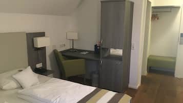 Una habitación de hotel con una cama, un escritorio, una silla, un armario y un pequeño banco.