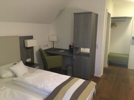 Una habitación de hotel con una cama, un escritorio, una silla, un armario y un pequeño banco.