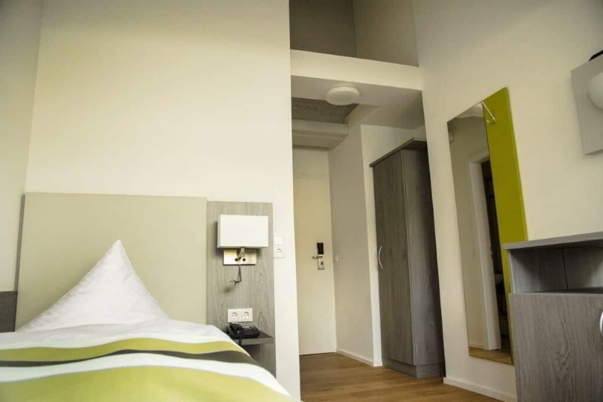 A hotel room with a bed, a bedside telephone, a wall-mounted light, and a wardrobe.