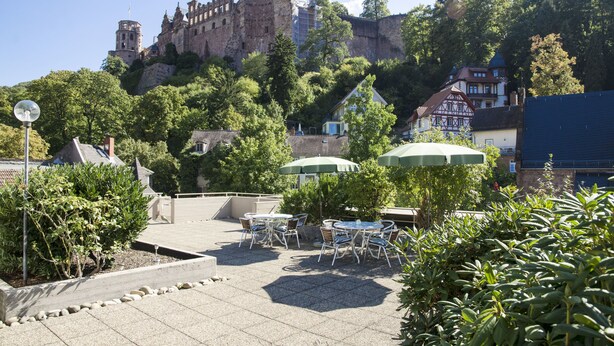 A courtyard with outdoor seating, a castle in the background, and a mix of traditional and modern buildings. - Hotel Am Schloss (Heidelberg)
