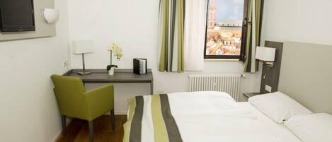 A hotel room with a bed, a desk, a chair, a TV, and a window with a view of a building.