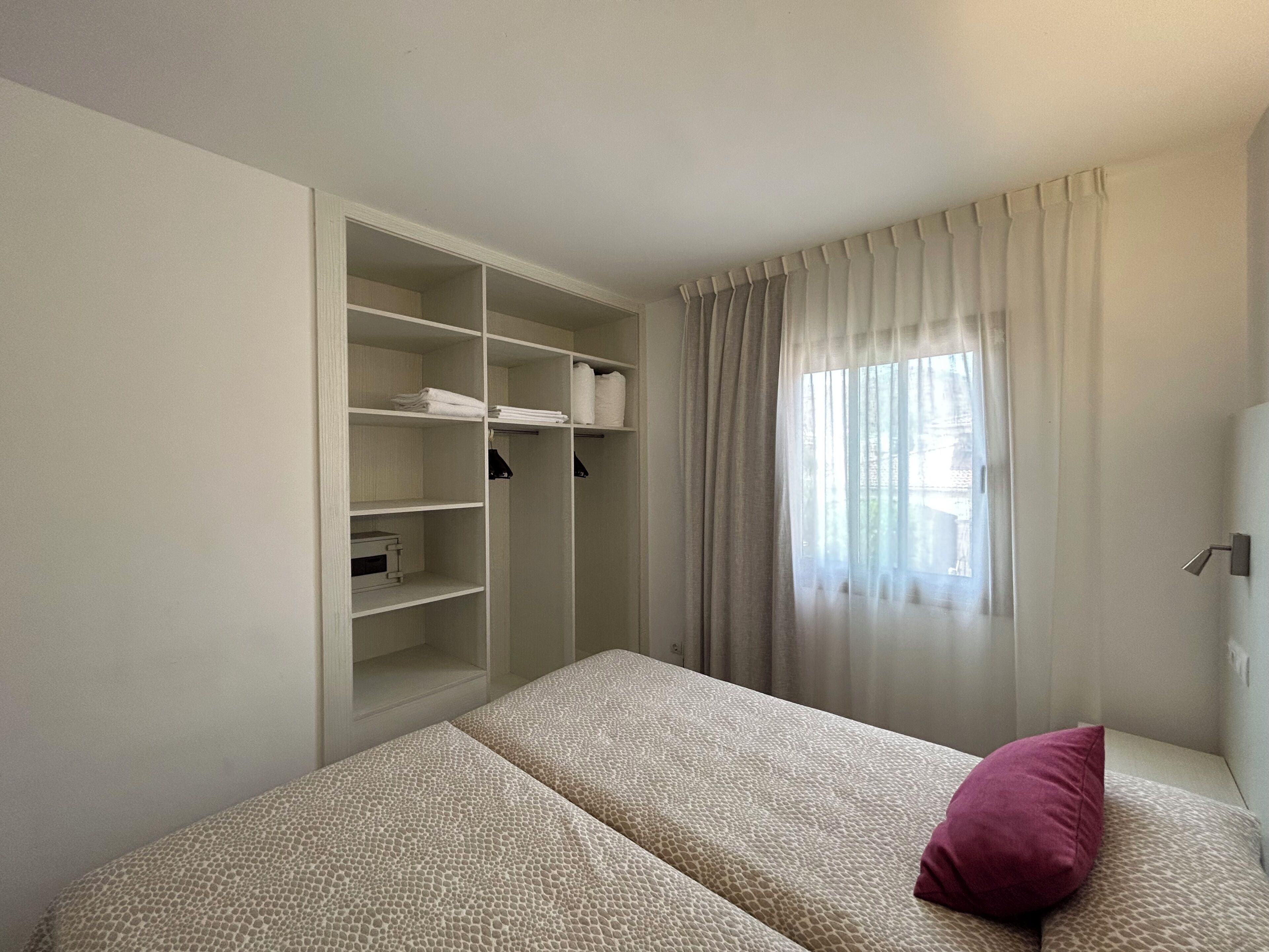 Quarto com cama, guarda-roupa e janela com cortinas.