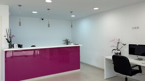 Un mostrador de recepción con decoración blanco y rosa, un monitor de computadora y una silla de oficina negra.