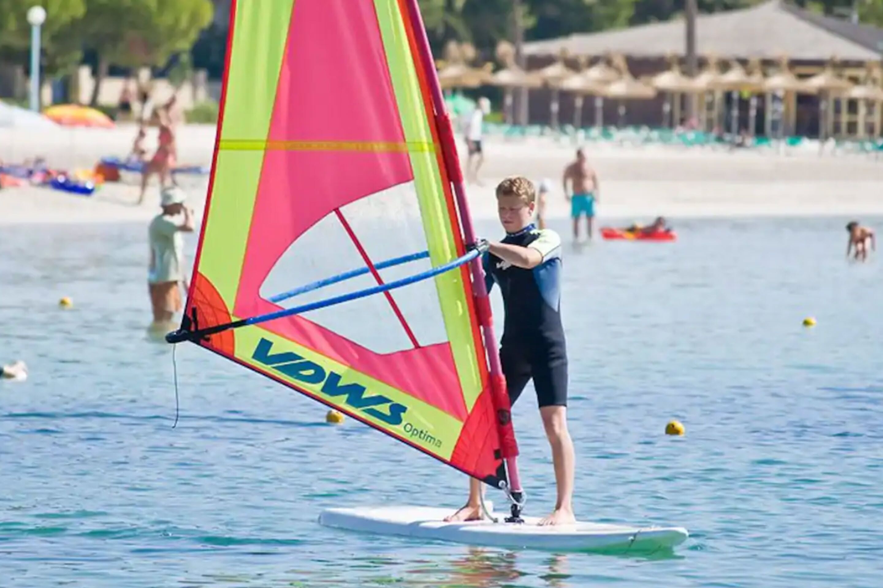 A person windsurfing on a clear day at a beach with a colorful sail.